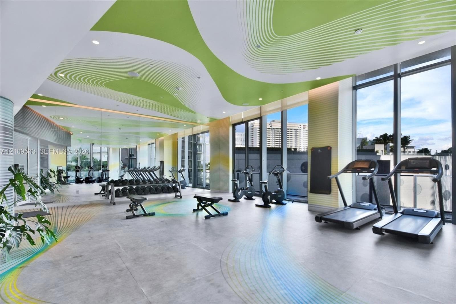 Expansive fitness area featuring floor-to-ceiling windows, large-format tile flooring, recessed lighting, and a custom patterned ceiling treatment