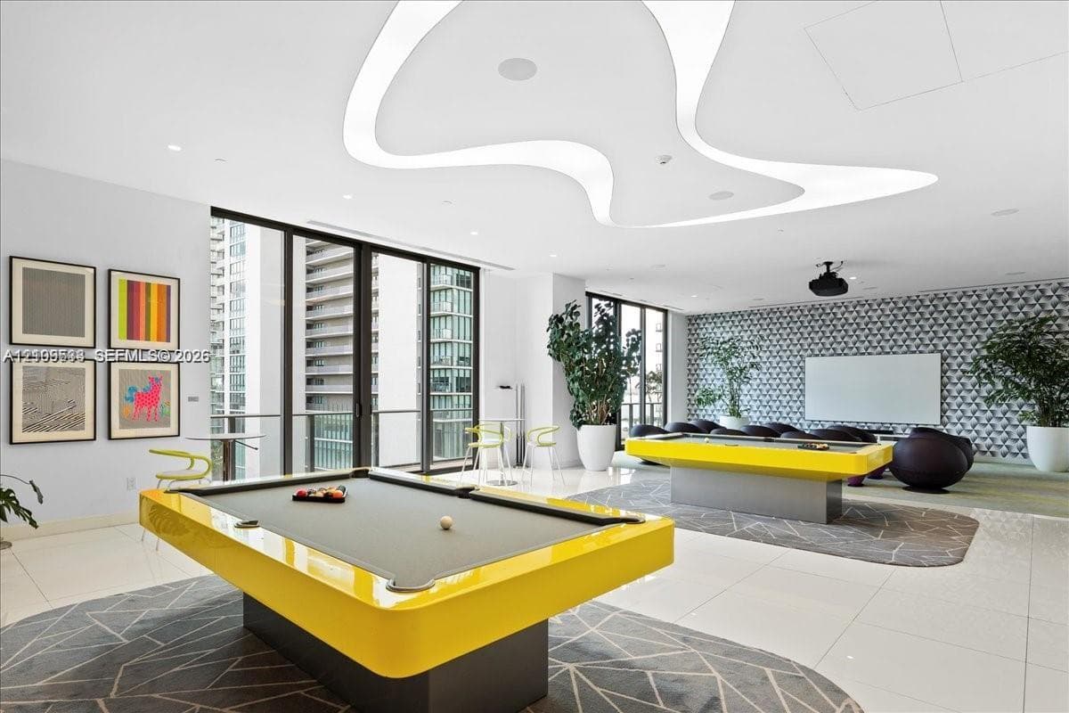Expansive recreational room featuring custom curvilinear recessed ceiling lighting, full-height glass doors, large-format tile flooring, and a patterned accent wall