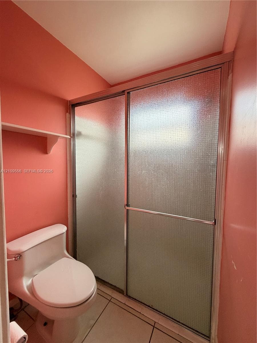 Shower enclosure with textured glass sliding doors and metal frame, white ceramic toilet, and tiled flooring