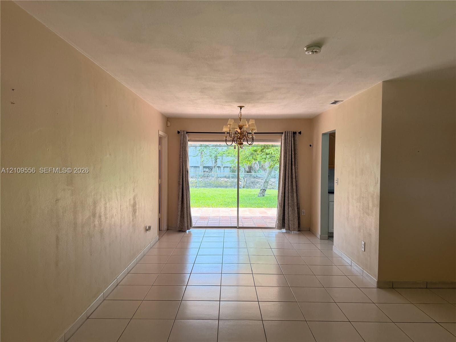 Large-format tile flooring, multi-arm chandelier, and sliding glass doors opening to an exterior patio