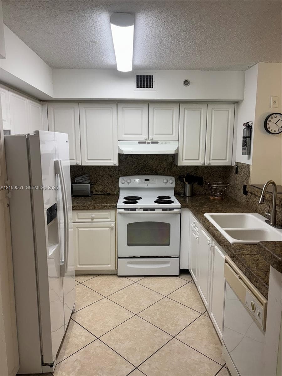 Kitchen featuring white cabinetry, stone-finish countertops, tile flooring, and white built-in appliances
