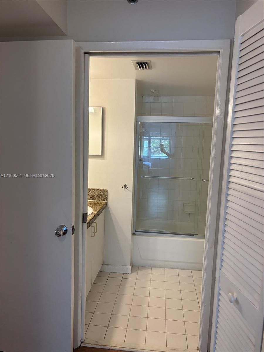 Bathroom featuring a tiled floor, stone-finish vanity countertop, and a shower-tub combination enclosed by sliding glass doors