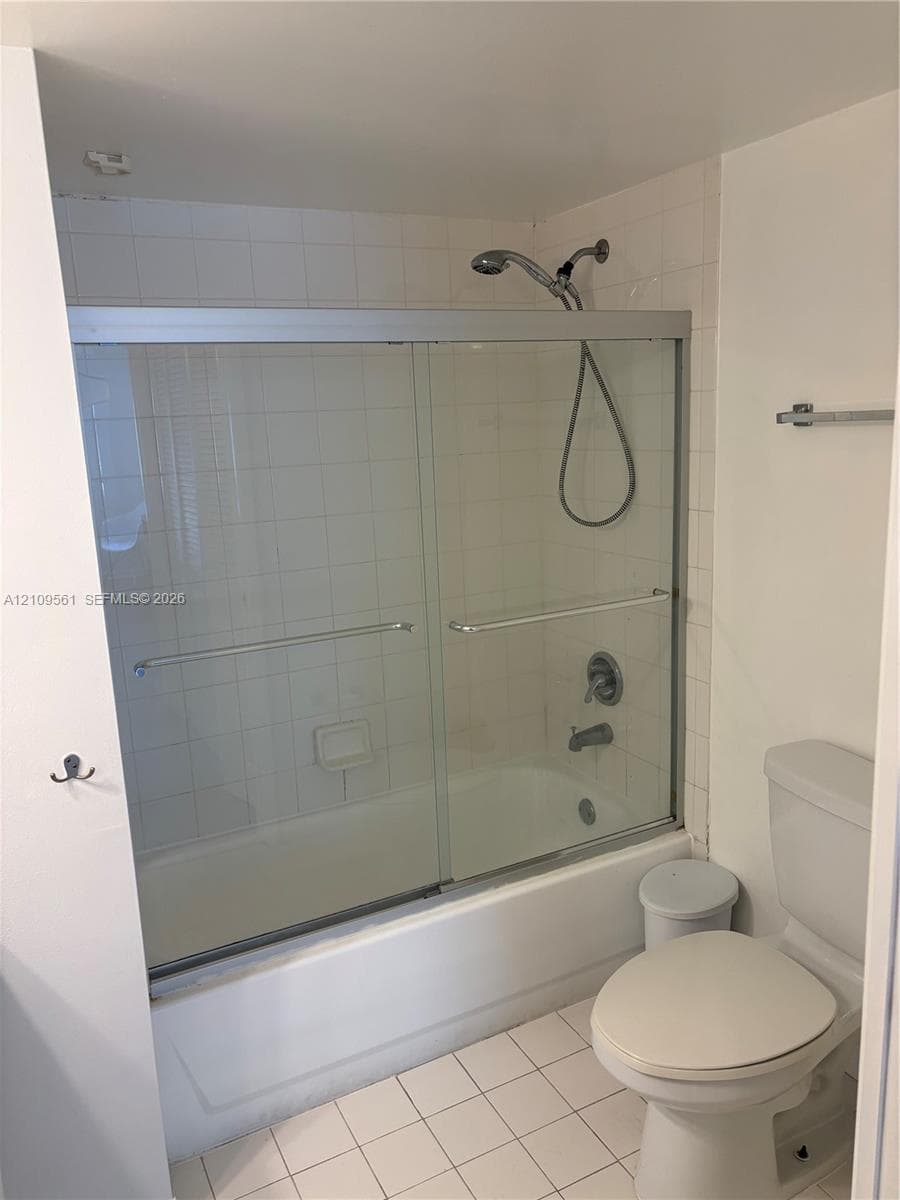 Bathtub and shower combination featuring a glass sliding enclosure, handheld shower fixture, white ceramic tile surround, and square-tile flooring