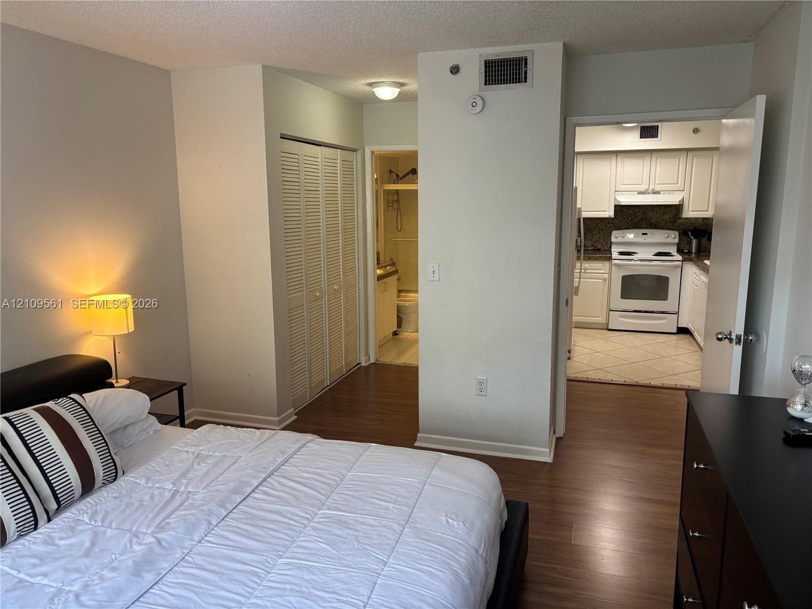 Wood-finish flooring throughout, closet with louvered double doors, flush-mount ceiling lighting, and kitchen equipped with white cabinetry and a white freestanding range