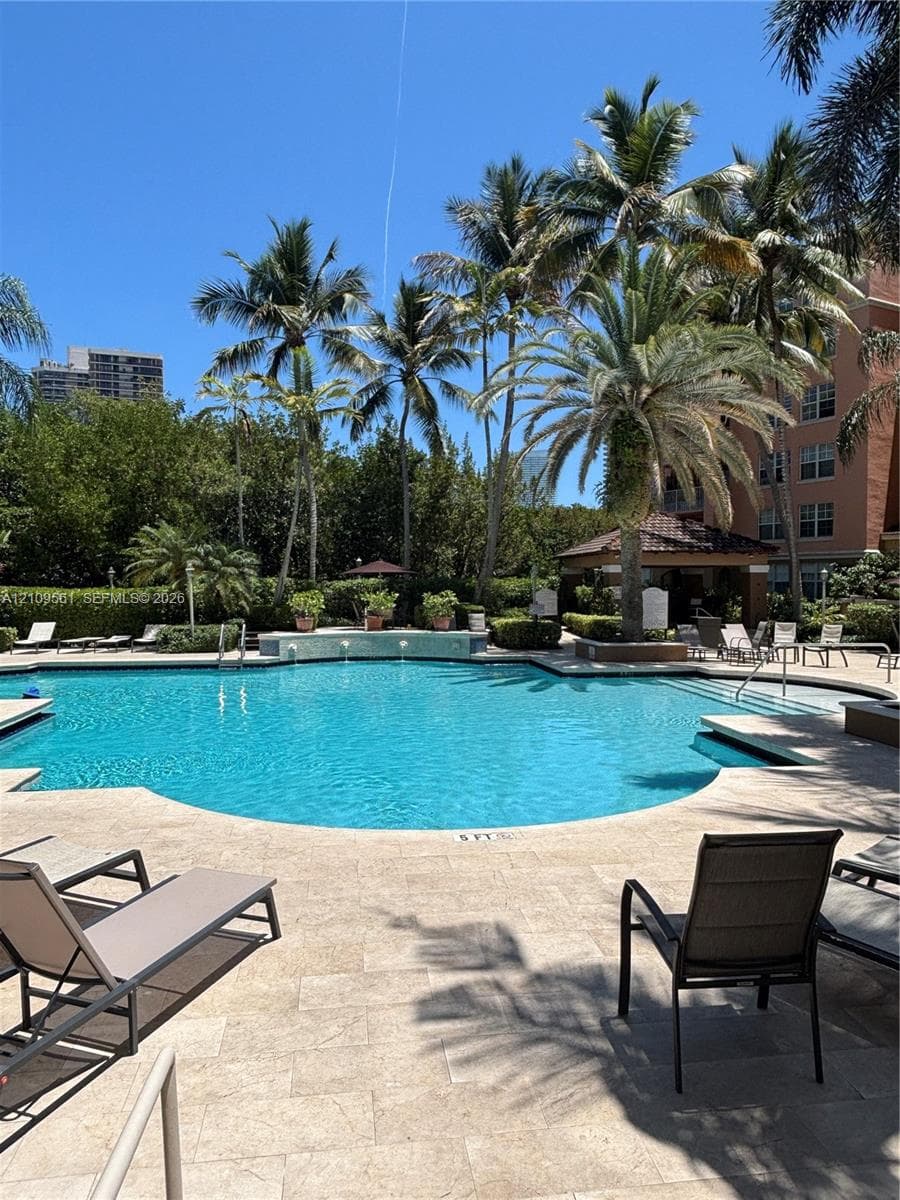 Swimming pool featuring a stone-tile deck, tiered waterfall feature, and surrounding mature palm trees