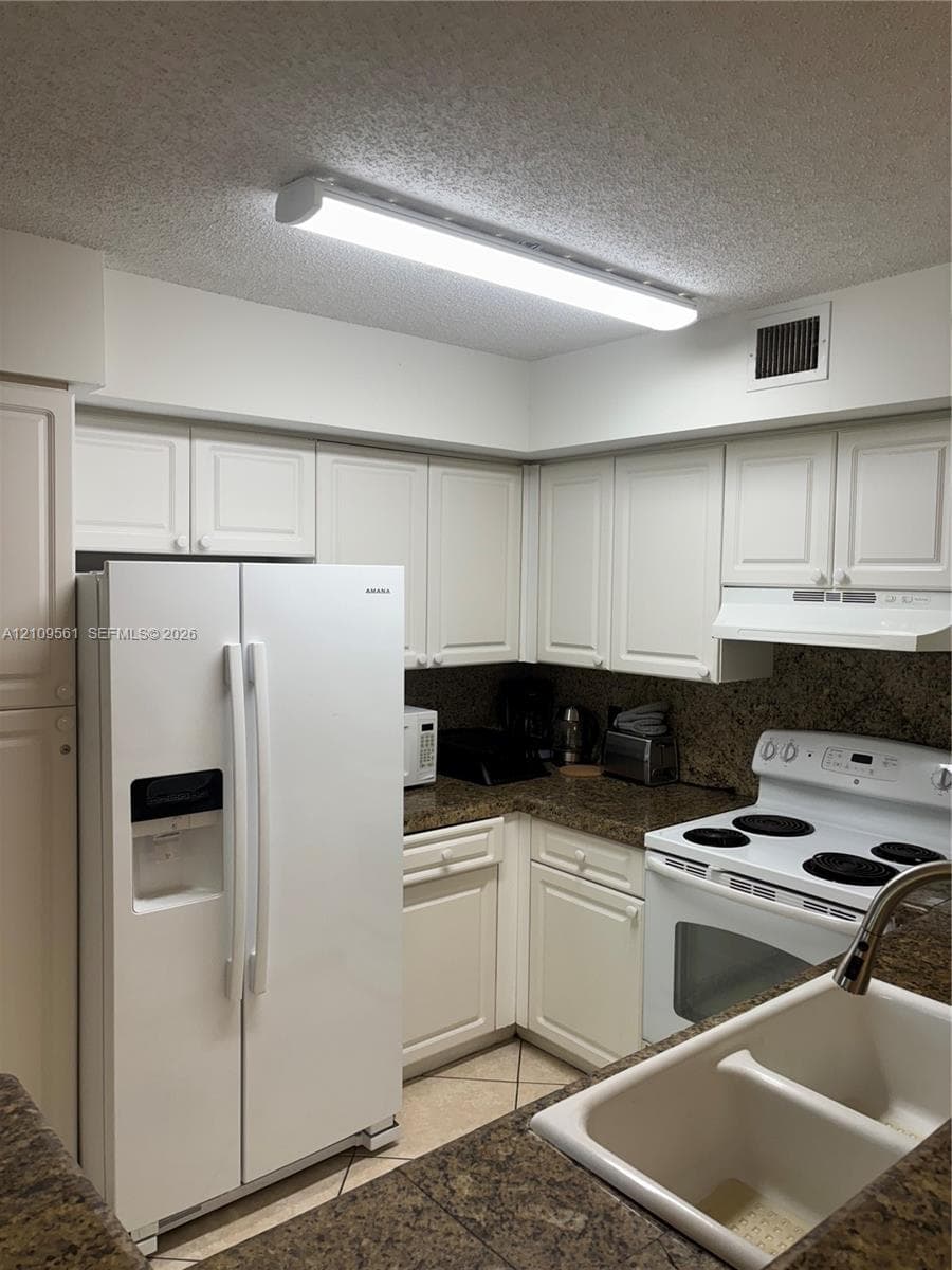Kitchen featuring white cabinetry, stone-finish countertops, dual-basin sink, and integrated white appliances