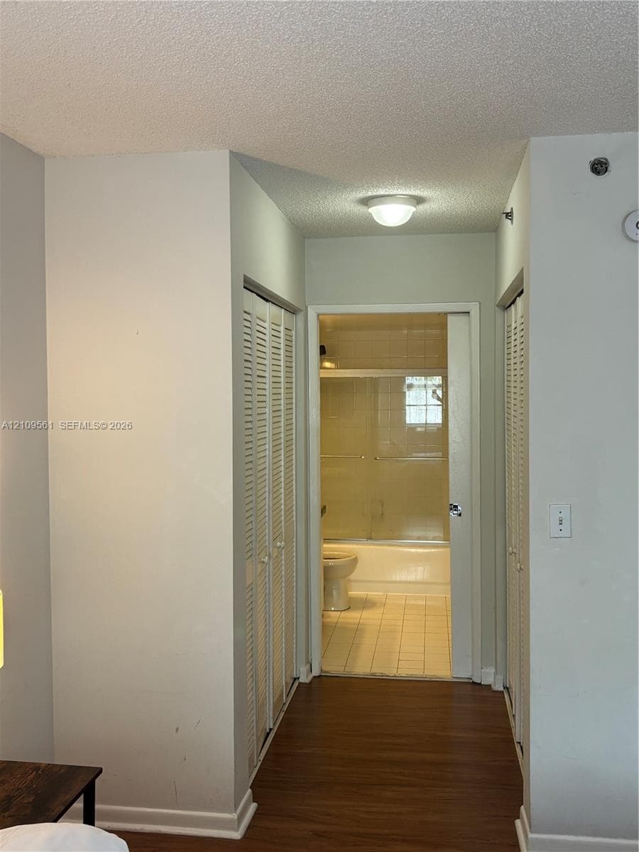 Wood-finish flooring, dual bi-fold closet doors, flush-mount ceiling lighting, and tiled bathroom flooring with an integrated shower-tub enclosure