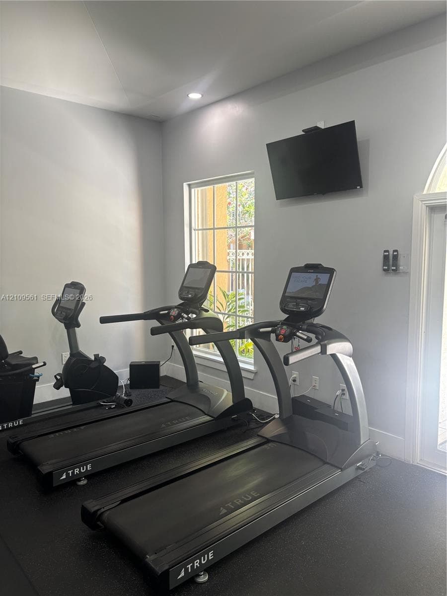 Dedicated fitness space featuring high-contrast wall-to-wall rubberized flooring, recessed lighting, and a wall-mounted flat-panel television