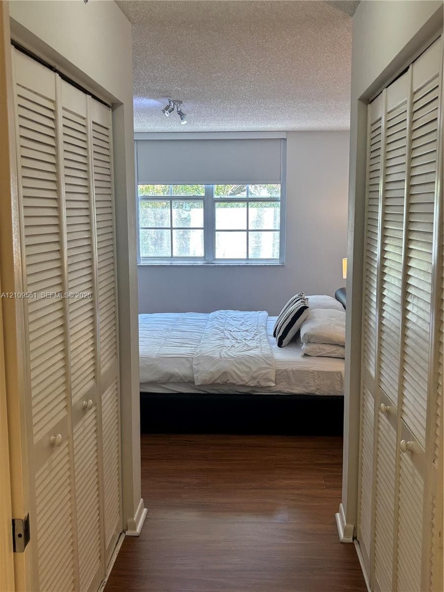 Dual floor-to-ceiling closets with white louvered bi-fold doors, wood-finish flooring, multi-pane window, and adjustable track lighting