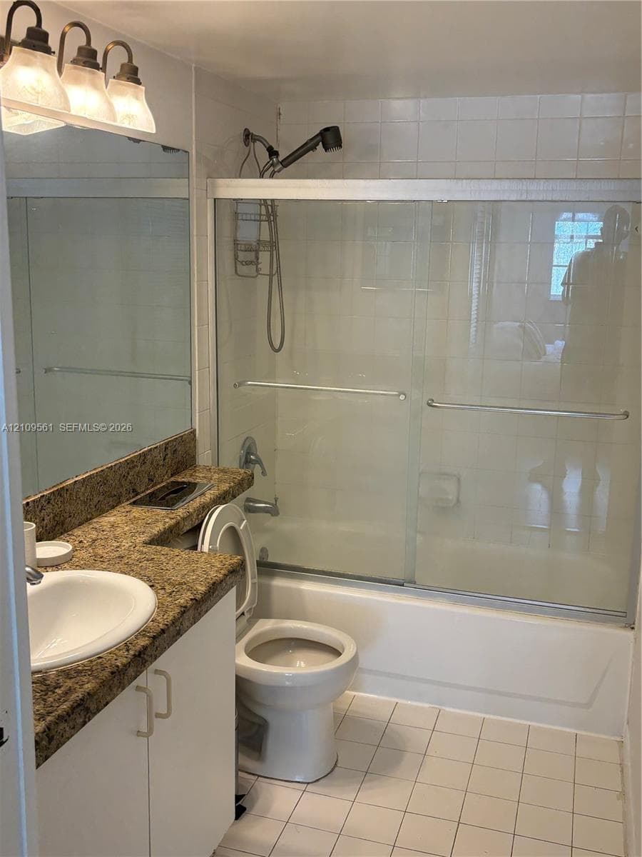 Bathroom featuring a stone-finish countertop, white cabinetry, a full-width vanity mirror, a tub-shower combination with sliding glass doors, and tiled flooring