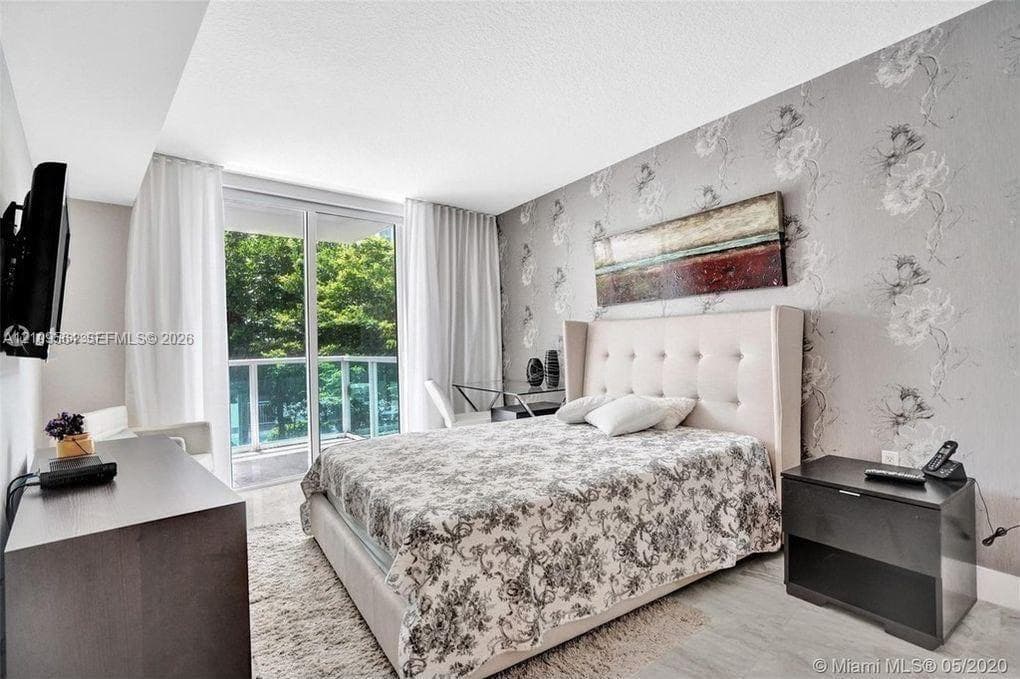 Floor-to-ceiling glass sliding doors opening to a balcony, patterned accent wall covering, and neutral light-toned flooring