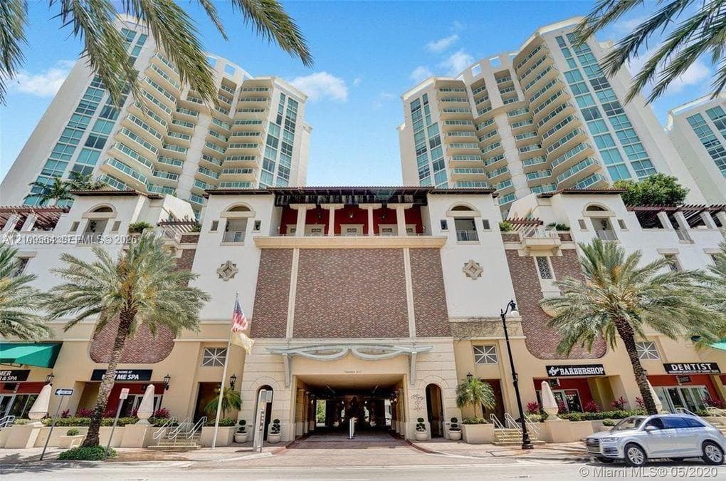 Multi-story high-rise architecture featuring glass balconies, brick-accented exterior masonry, arched entryways, and integrated ground-floor commercial spaces