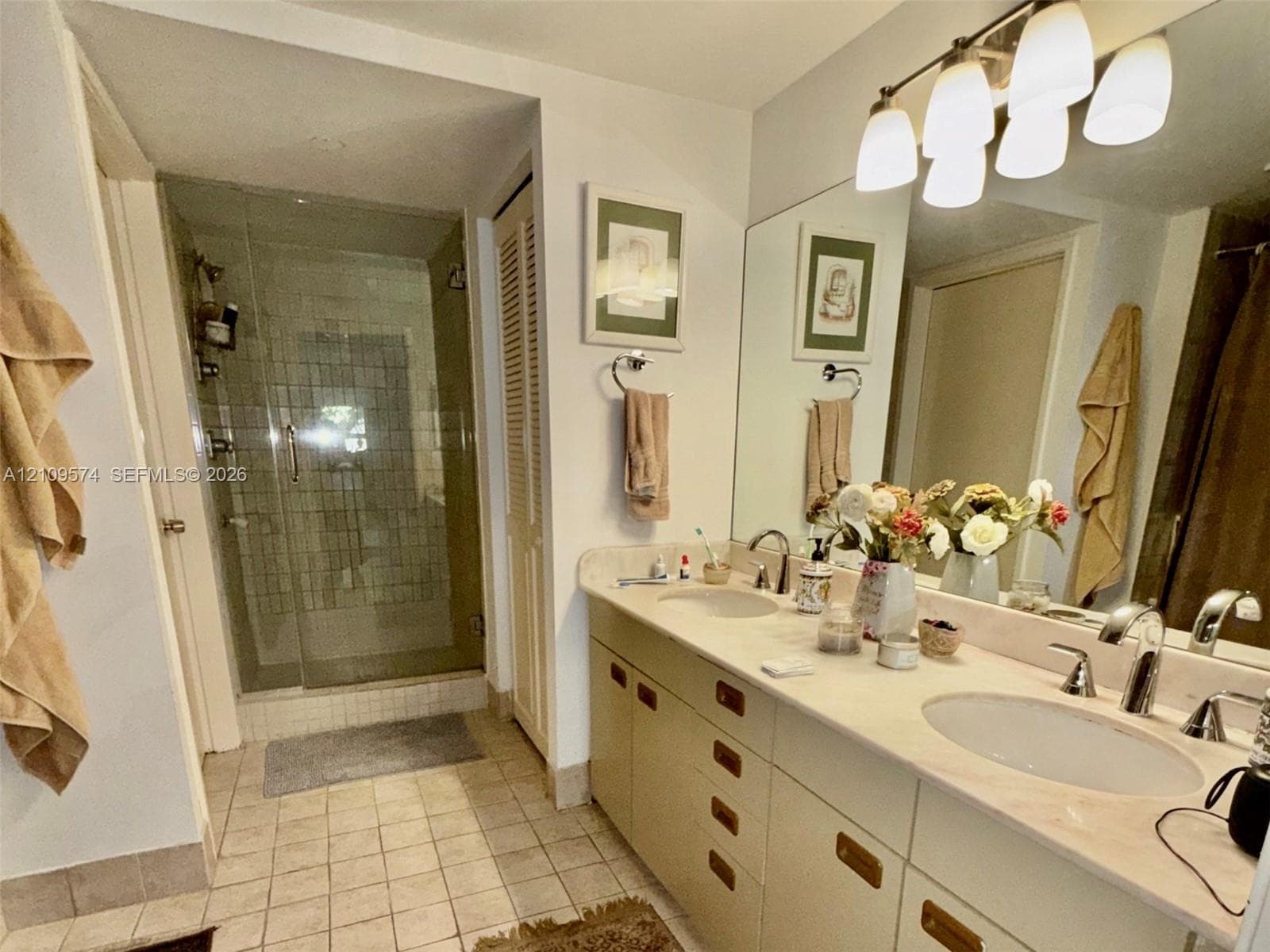 Double vanity featuring integrated sinks, light-toned countertop, and substantial cabinetry, complemented by a glass-enclosed shower with tiled surround and multi-light wall fixture