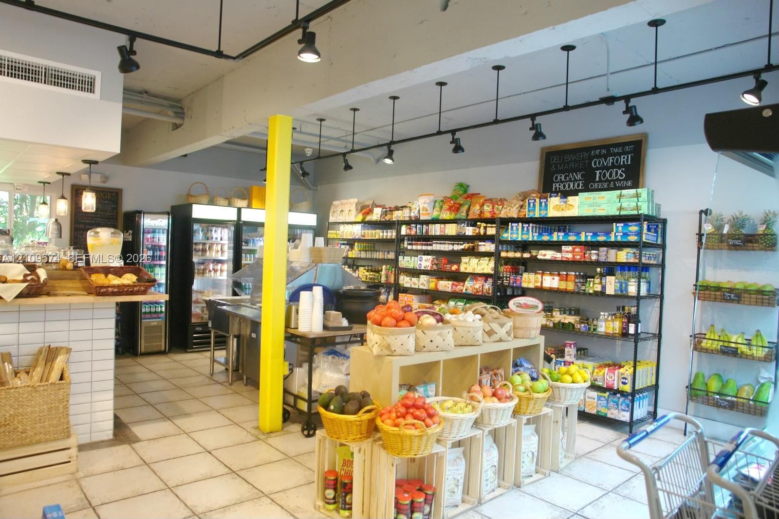 Commercial space featuring industrial-style track lighting, square tile flooring, exposed ceiling beams, built-in white tiled service counter, and floor-to-ceiling metal shelving
