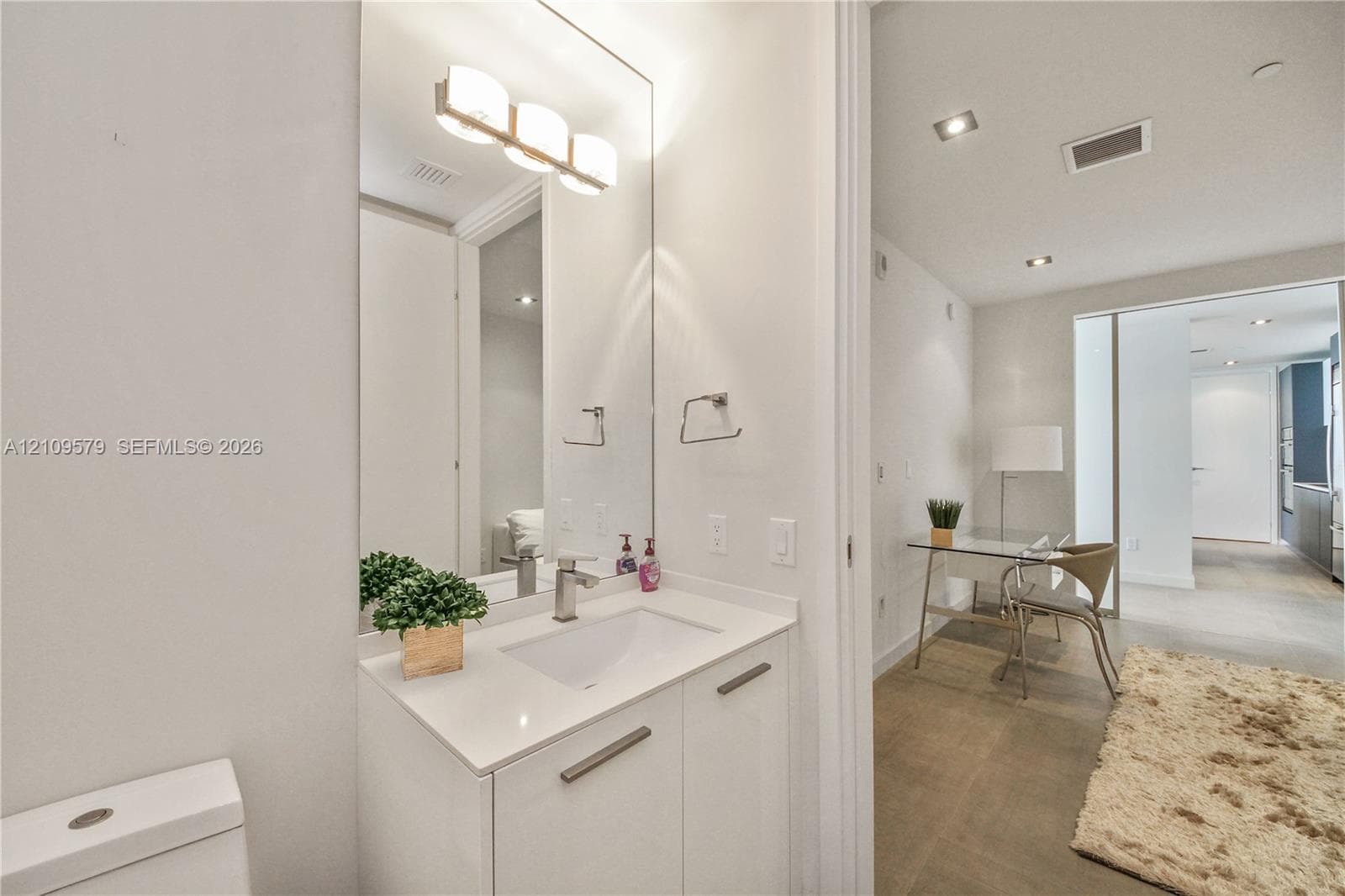 Bathroom vanity with a stone countertop, integrated basin, brushed metal hardware, and an expansive wall-mounted mirror with multi-light fixture