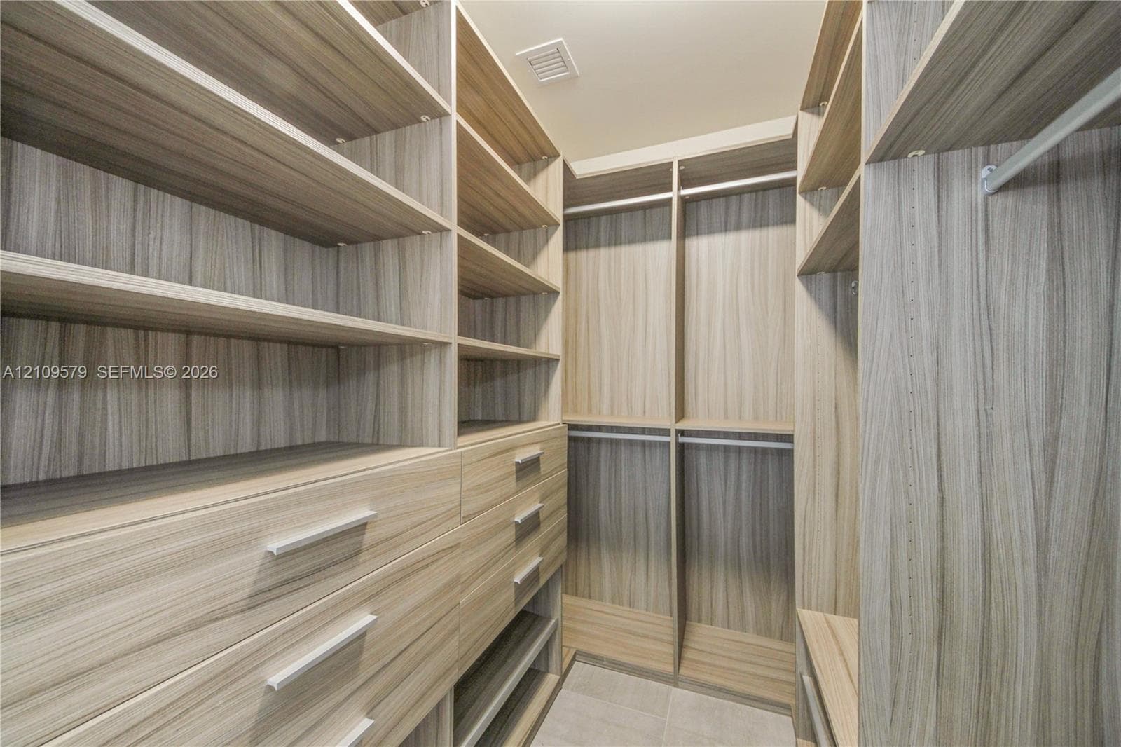 Walk-in closet featuring custom wood-finish cabinetry, built-in shelving, multiple pull-out drawers with metal hardware, and dual hanging rods