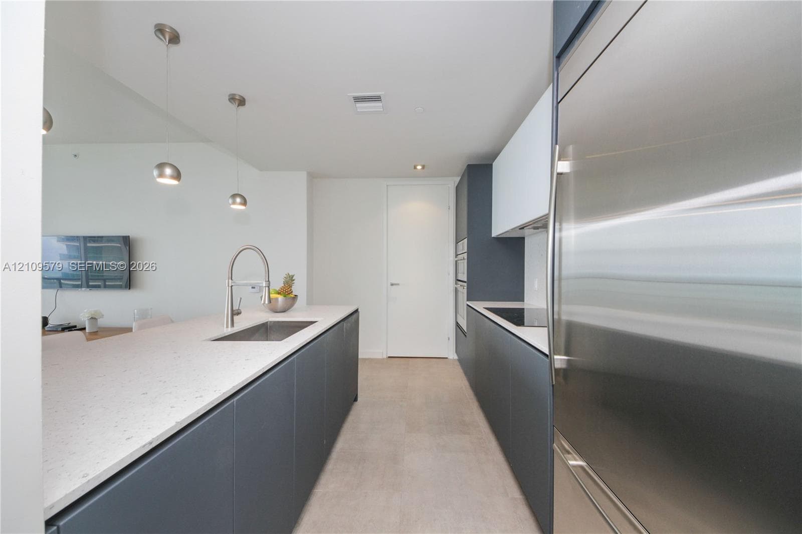 Modern kitchen featuring matte charcoal cabinetry, light-toned composite countertops, a stainless steel undermount sink with a high-arc pull-down faucet, integrated stainless steel appliances, and minimalist pendant lighting