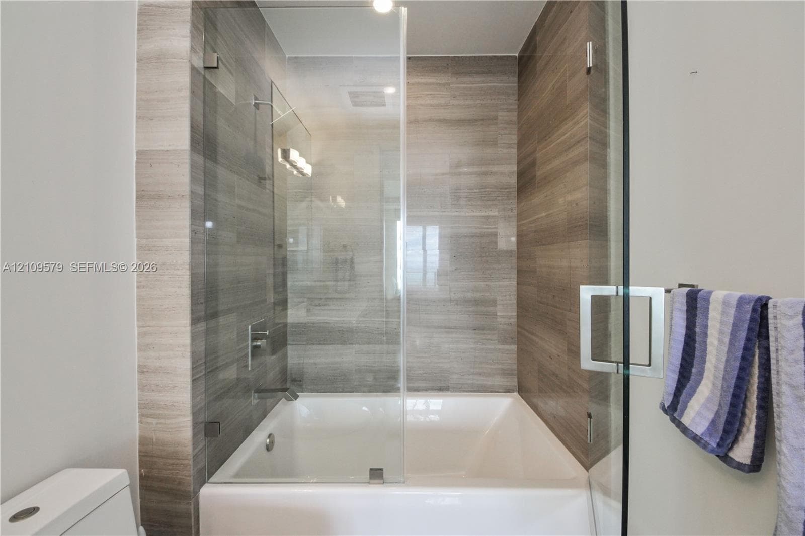 Shower-tub combination featuring floor-to-ceiling stone-tile surround, frameless glass panel, and polished chrome fixtures