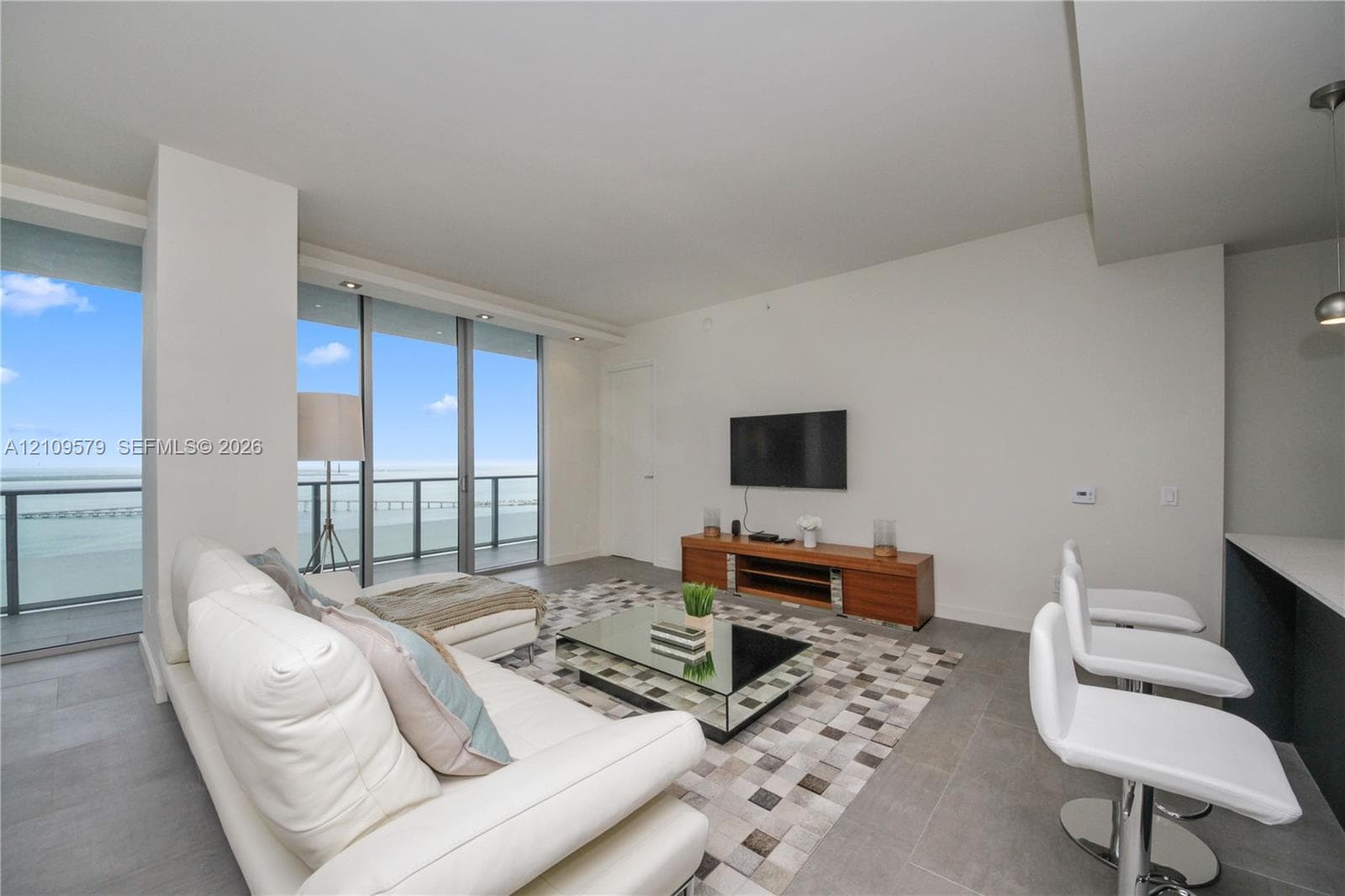 Living area featuring floor-to-ceiling glass sliding doors, private balcony with metal railing, large-format tile flooring, and integrated recessed lighting