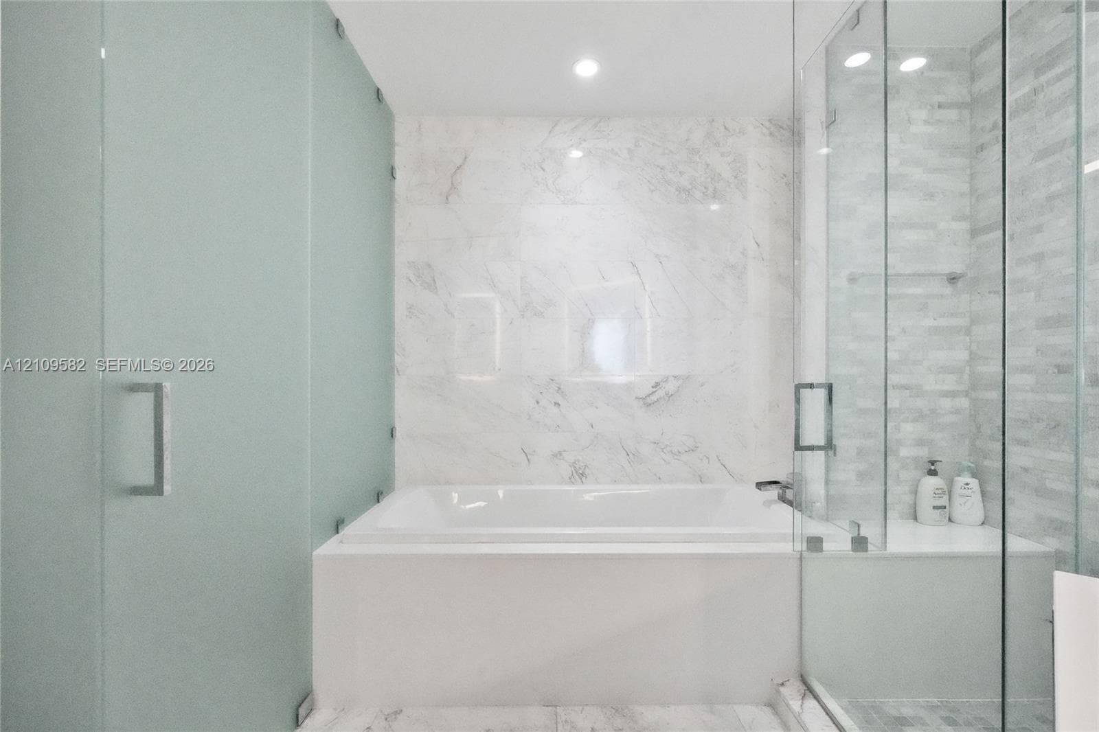 Soaking tub with stone-finish surround, glass-enclosed shower featuring tile walls, and recessed lighting