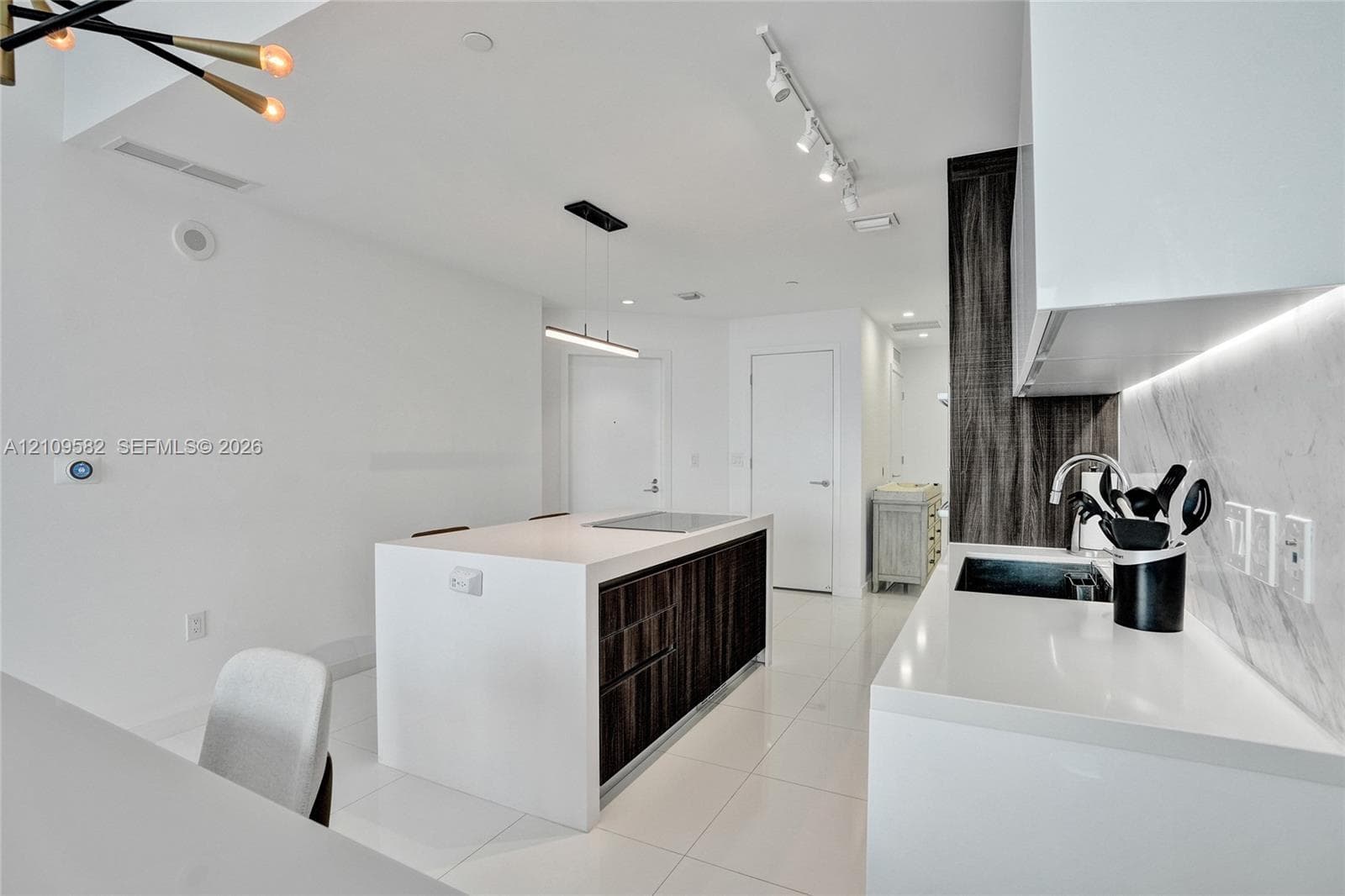 Kitchen featuring a waterfall-edge island with built-in cooktop, high-gloss white cabinetry, integrated under-cabinet lighting, tile backsplash, and polished flooring