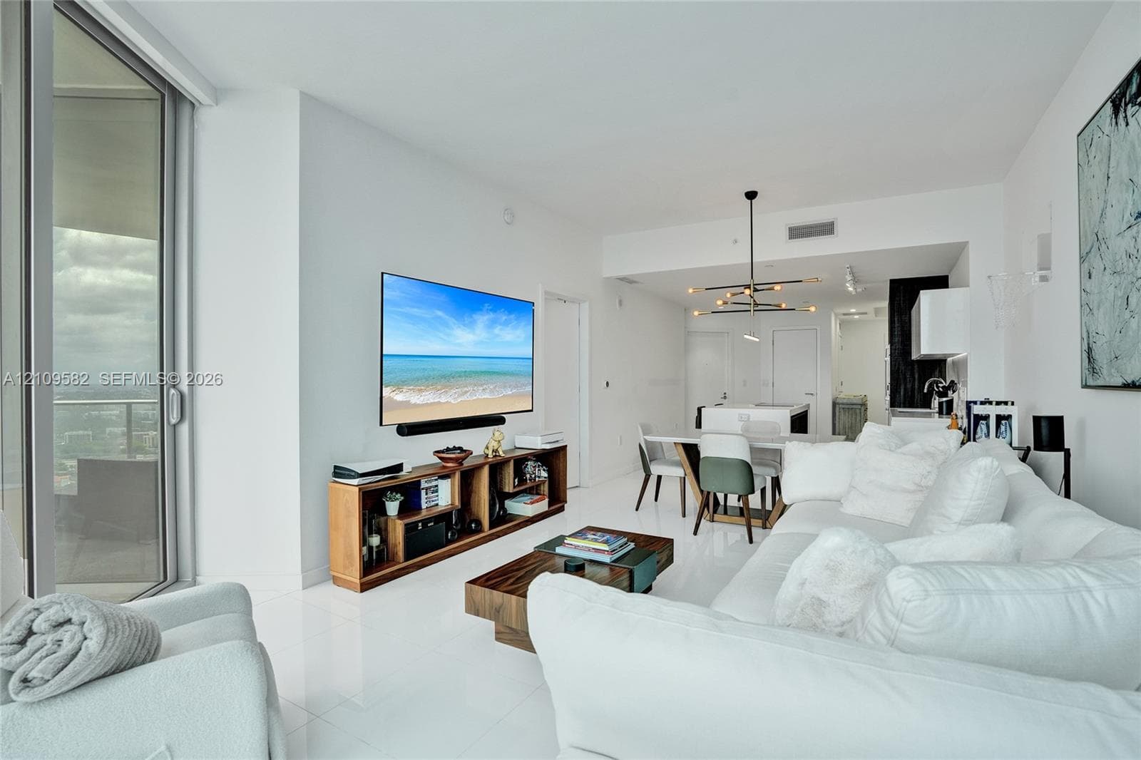 Open-concept interior featuring polished white flooring, floor-to-ceiling glass sliding doors, and a multi-arm modern light fixture