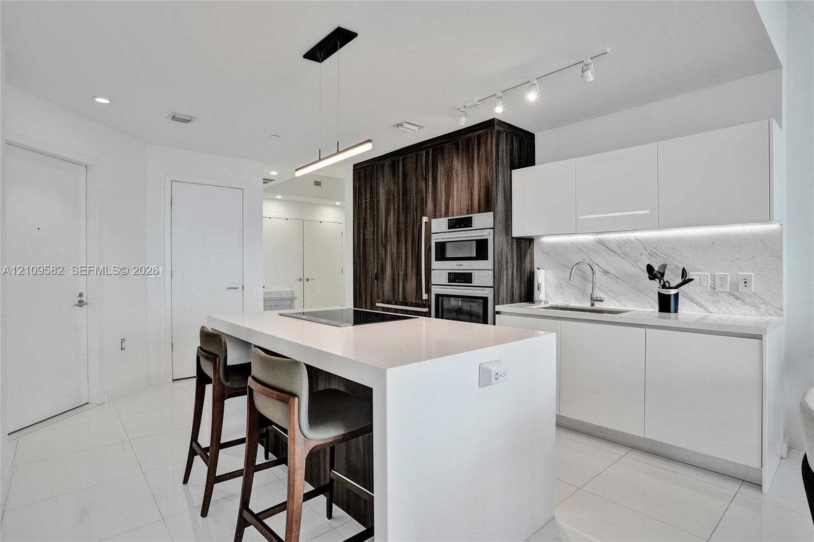 Kitchen featuring a central island with a quartz countertop, flat-panel cabinetry, a built-in wall oven and microwave, stone-finish backsplash, and integrated under-cabinet lighting