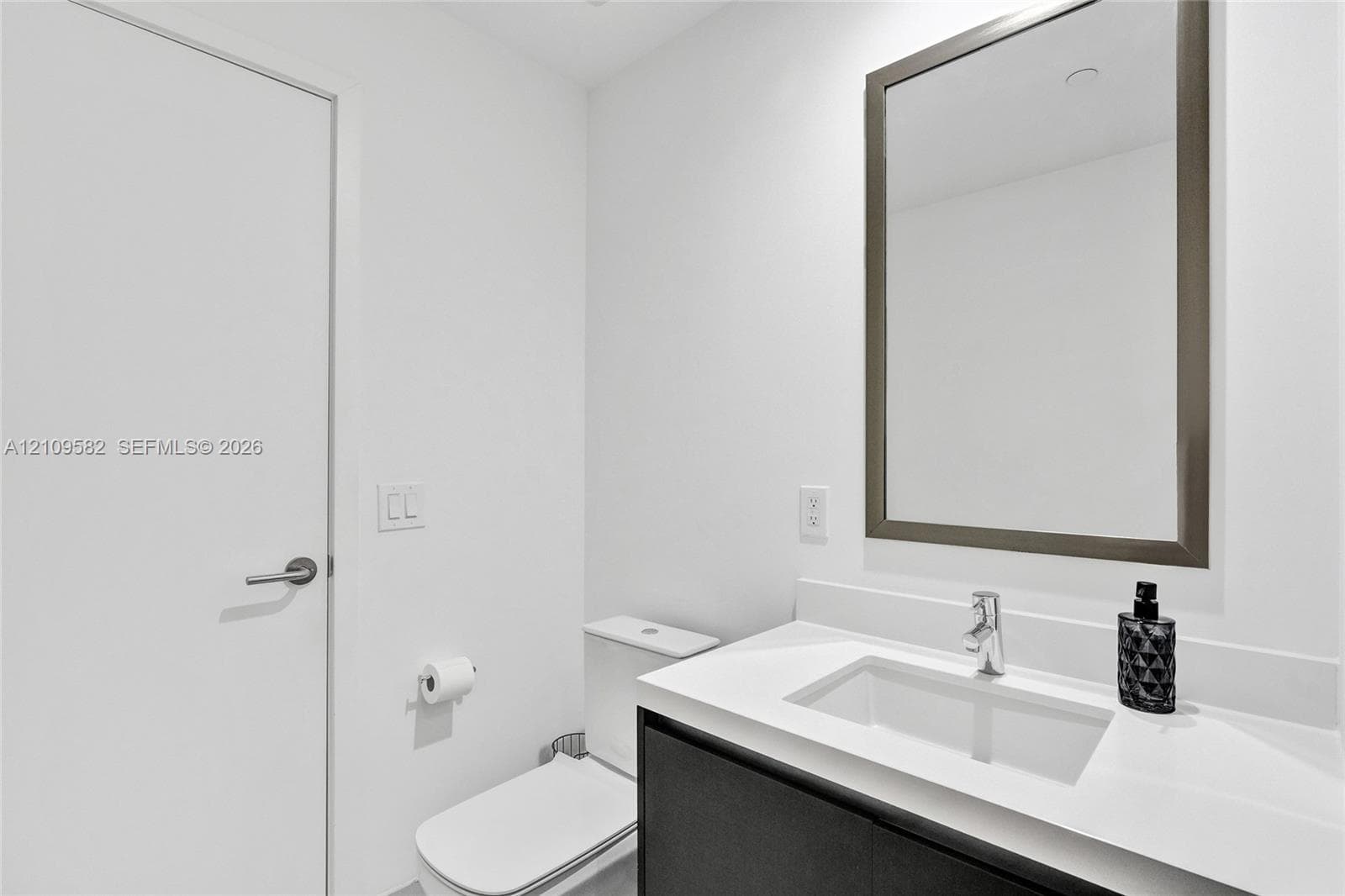 Modern vanity with a light-toned countertop, rectangular undermount sink, chrome faucet, and dark-finish base cabinetry, accompanied by a framed mirror