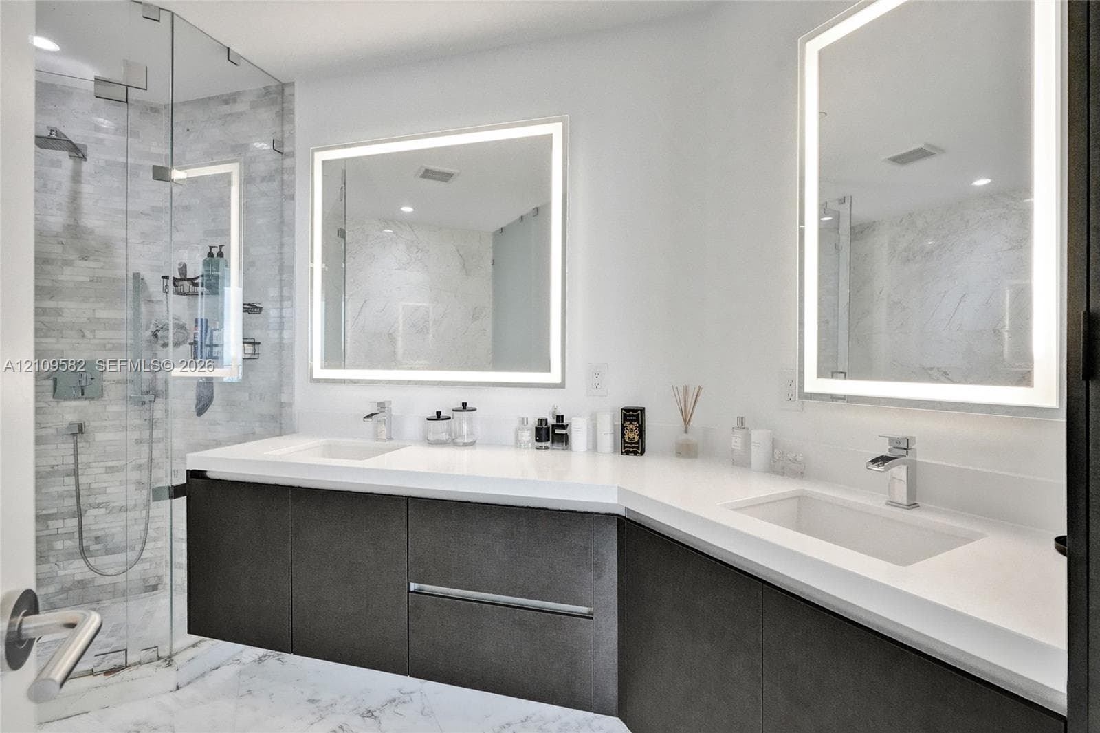 Floating vanity with dual rectangular undermount sinks, quartz countertop, frameless glass shower enclosure with textured tile walls, and two LED-backlit vanity mirrors