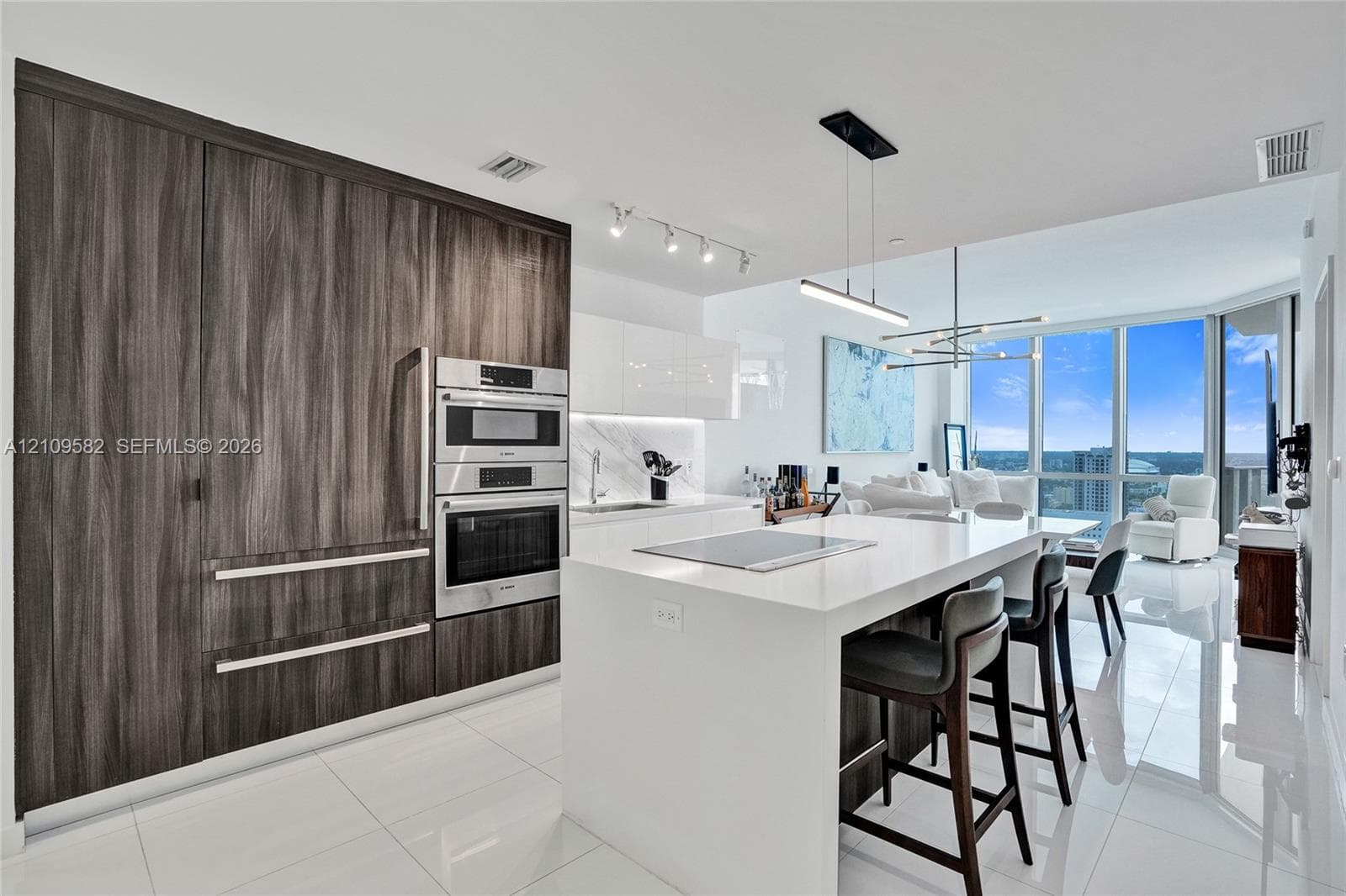 Contemporary kitchen featuring white solid-surface countertops, floor-to-ceiling wood-finish cabinetry, stainless steel wall-mounted appliances, and glass floor-to-ceiling windows