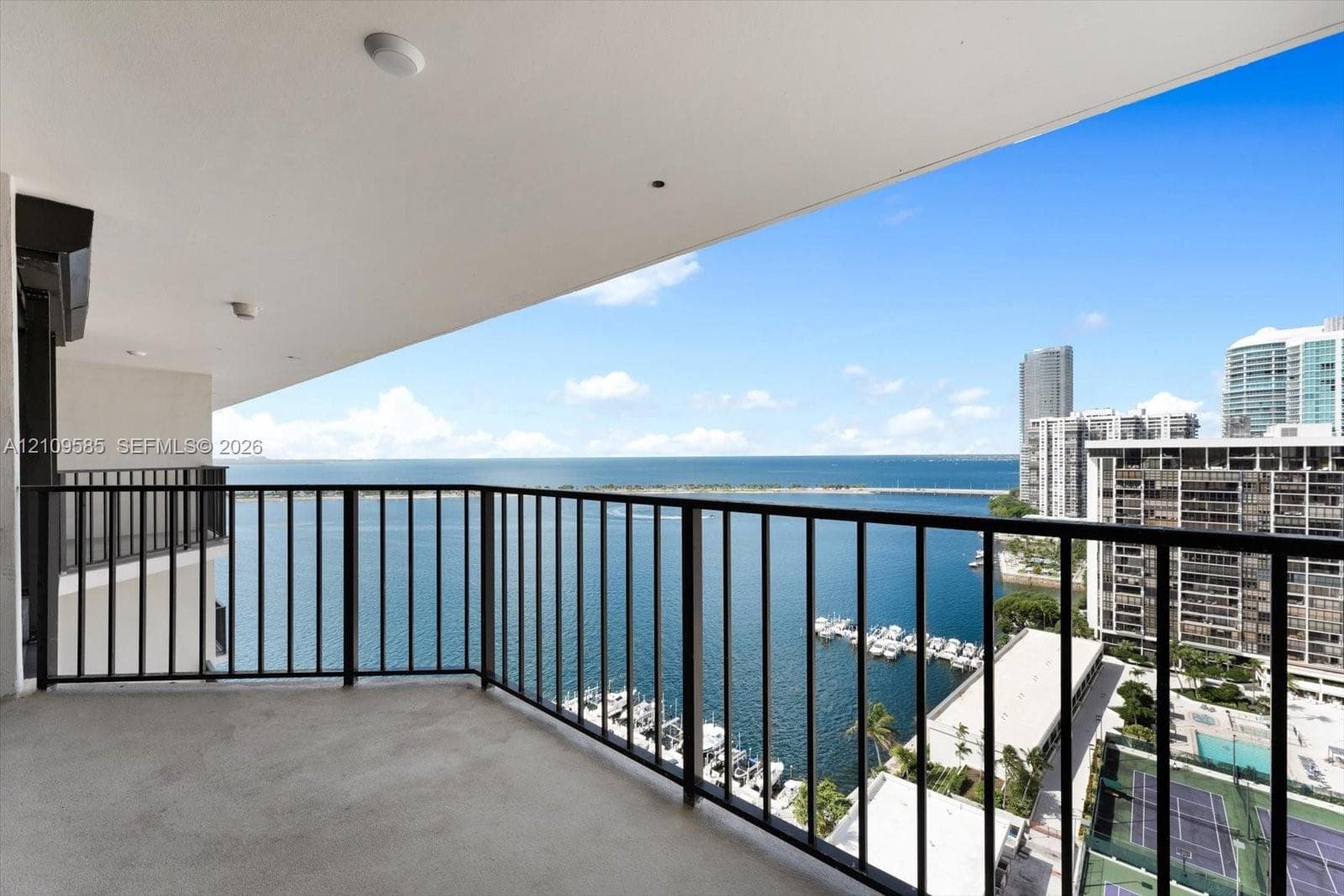 Covered balcony with black metal railing, concrete flooring, and water frontage