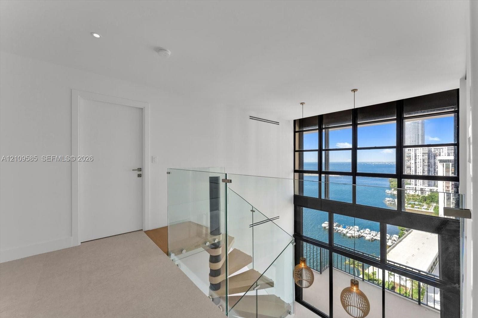 Double-height floor-to-ceiling windows featuring water frontage, architectural spiral staircase with wood-finish treads, glass panel railing, and integrated pendant lighting