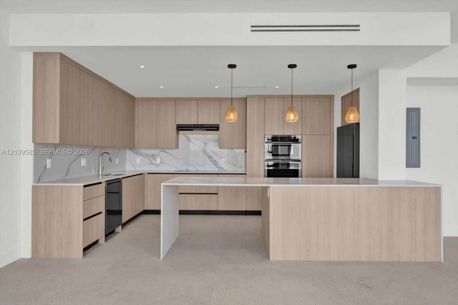 Kitchen featuring light wood-finish cabinetry, waterfall-edge island, stone-patterned backsplash, built-in double oven, and pendant lighting