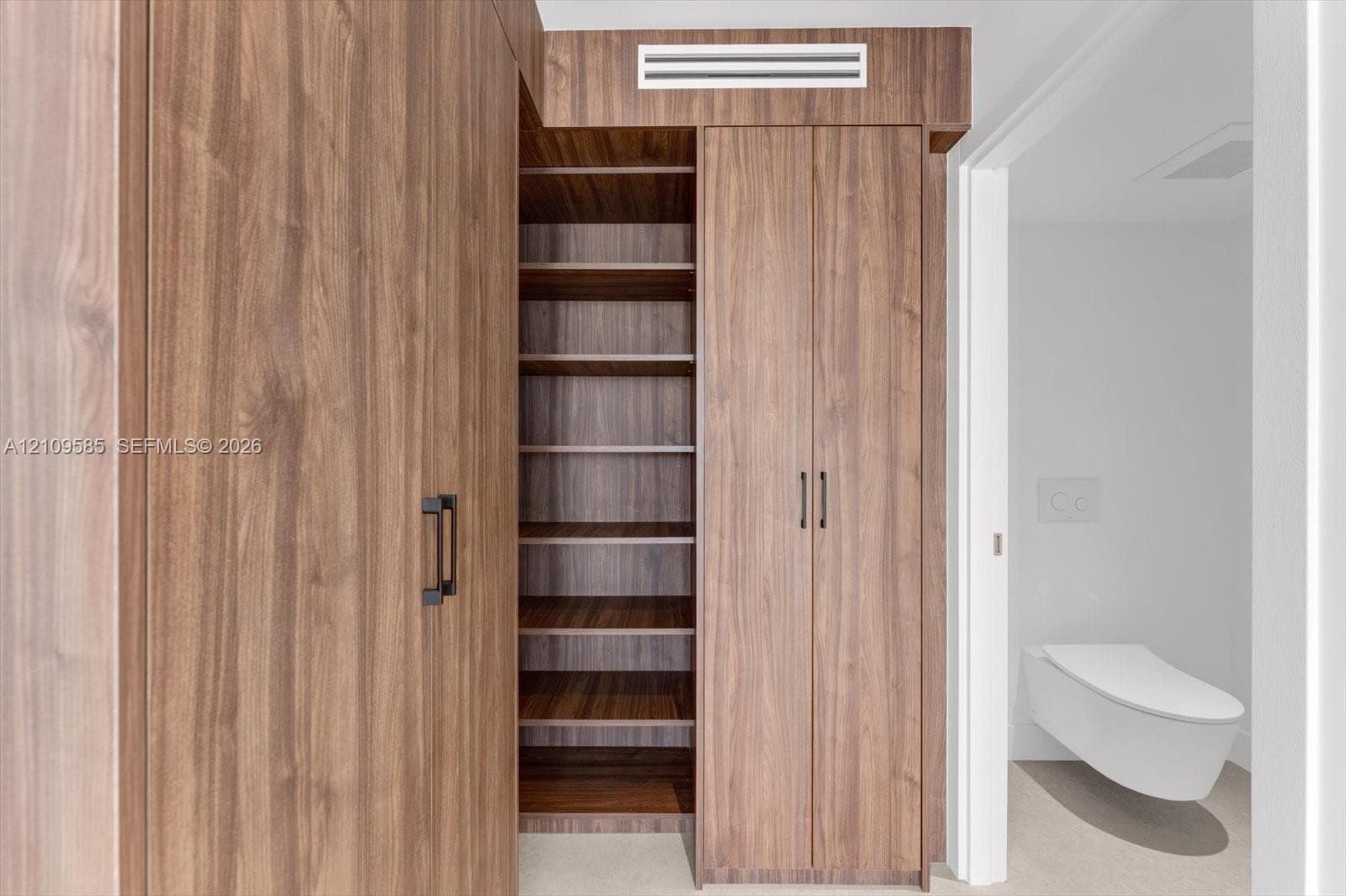 Floor-to-ceiling wood-finish cabinetry featuring open shelving, double-door storage, matte black hardware, and a wall-mounted toilet