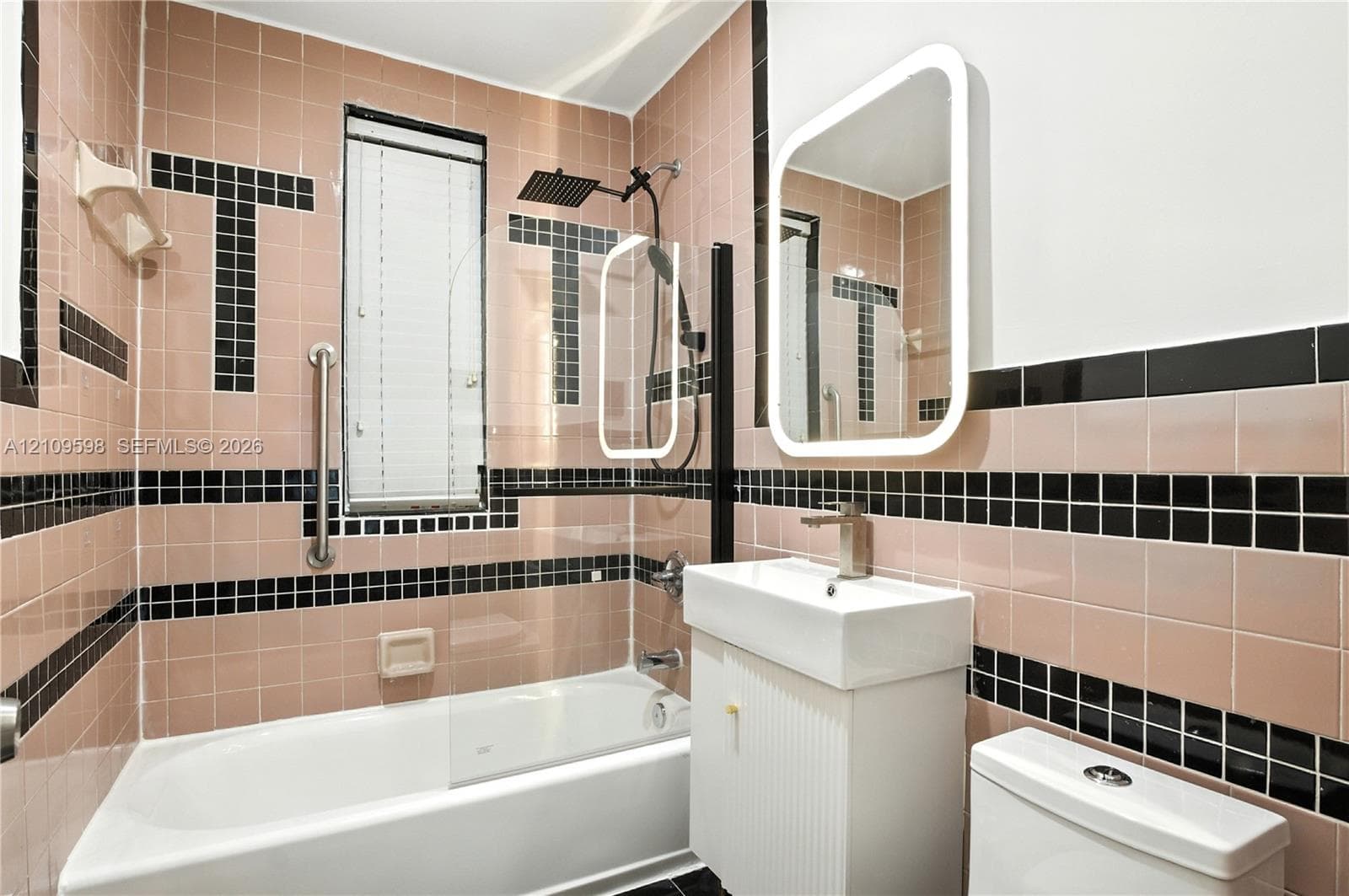 Bathroom featuring pink and black tiled walls, a glass shower partition with a rain-style showerhead, a pedestal sink with a metallic finish faucet, and an illuminated wall-mounted mirror