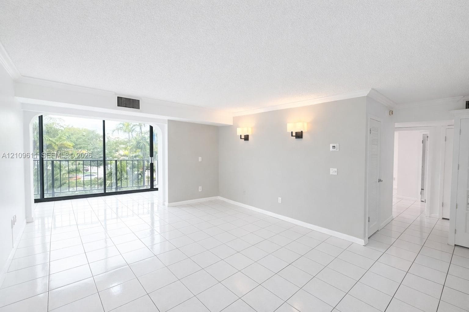Open-concept room featuring white ceramic tile flooring, floor-to-ceiling glass sliding doors, crown molding, and wall-mounted light fixtures