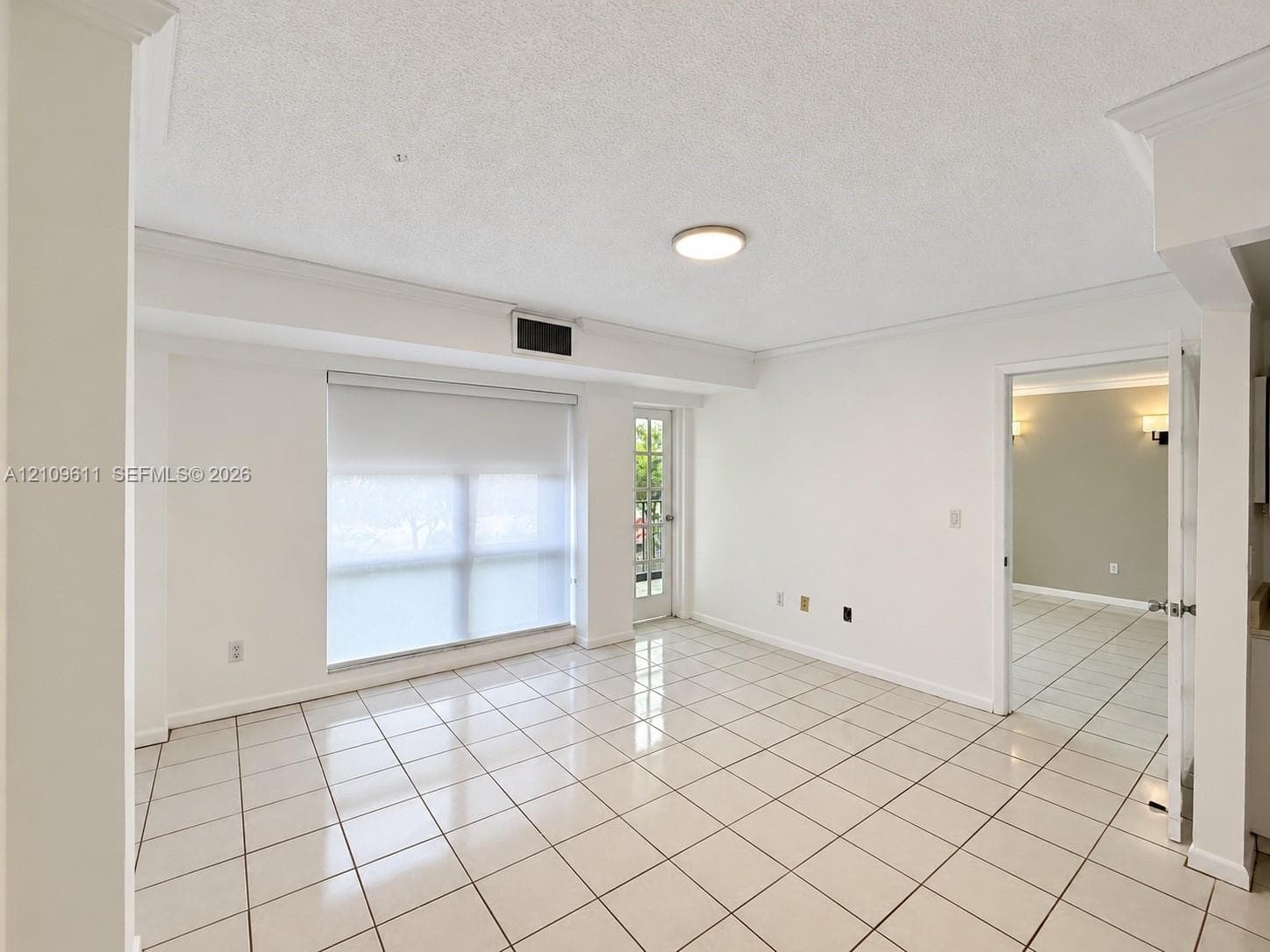 Interior space featuring large-format ceramic tile flooring, neutral wall finishes, crown molding, a multi-pane glass door, and a built-in recessed ceiling light fixture