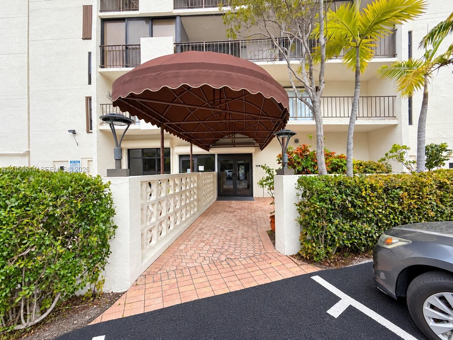 Covered building entrance featuring a brown fabric canopy, paved walkway, decorative concrete block wall, and integrated exterior lighting