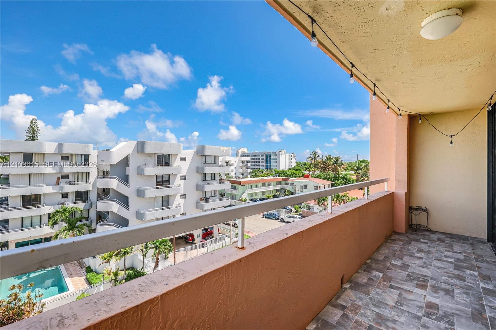 Covered balcony featuring multi-tone tile flooring, a white metal railing, and a ceiling-mounted light fixture