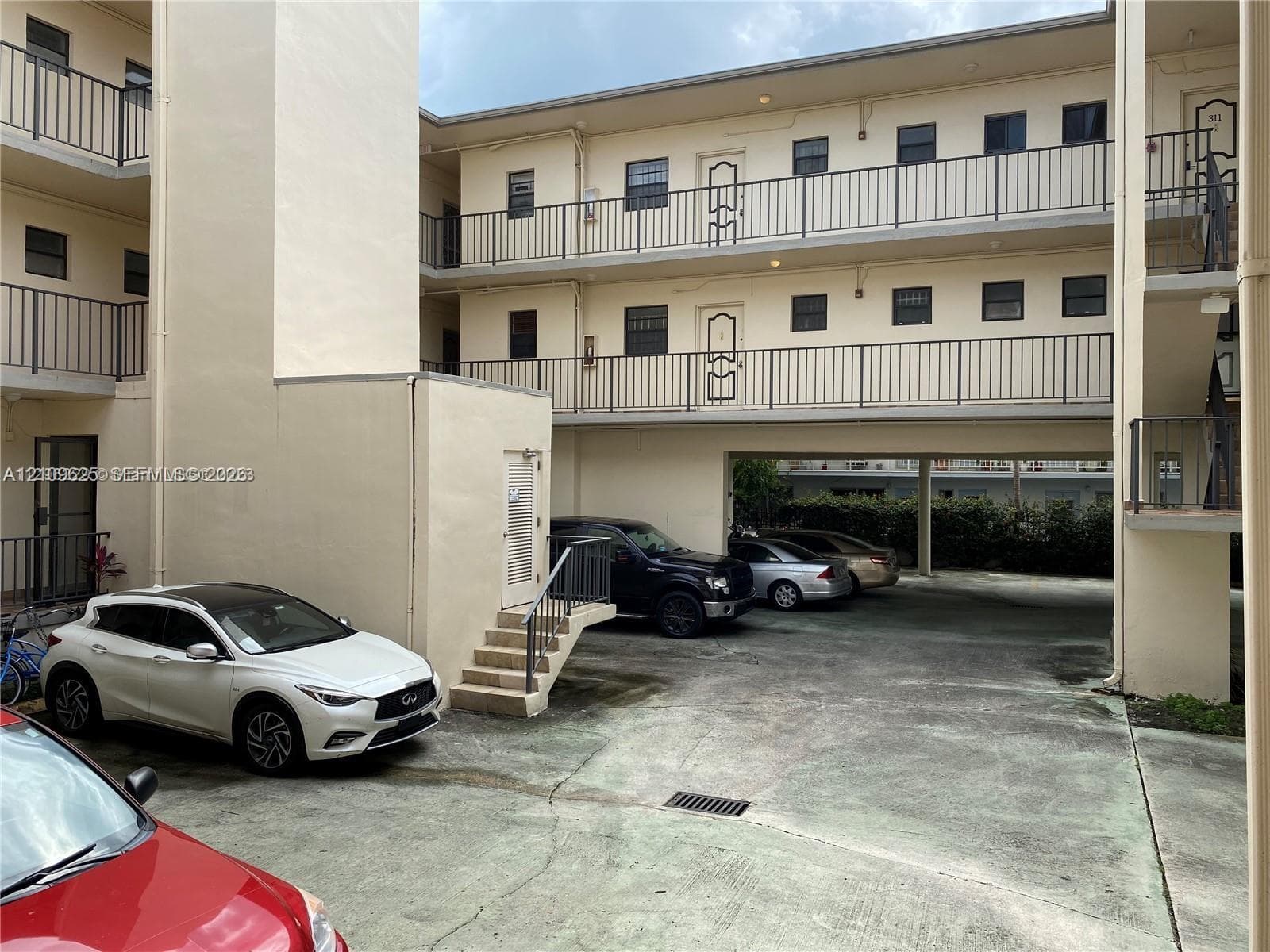 Multi-story exterior featuring a concrete parking level with covered areas, metal stairways, and balcony railings
