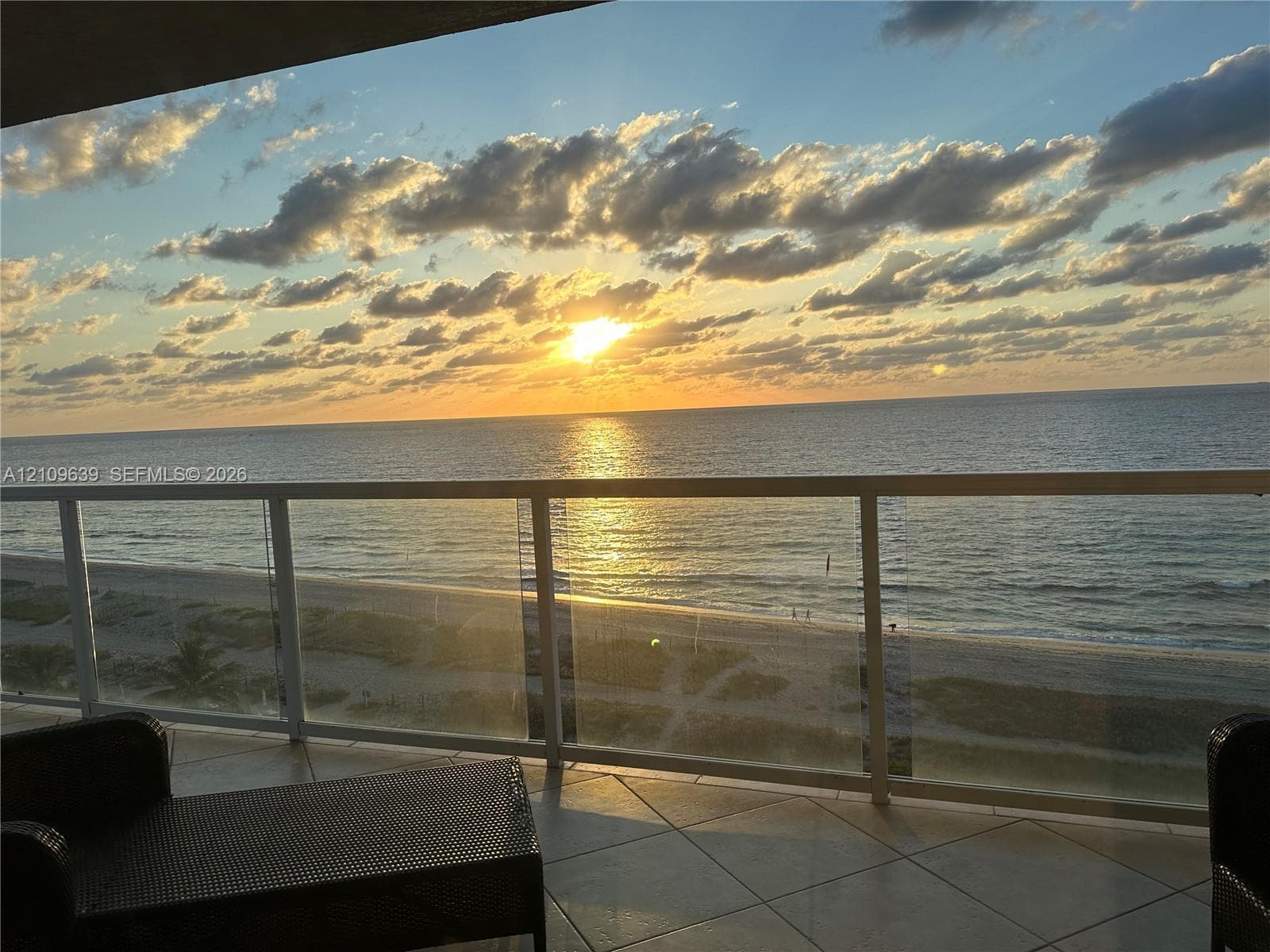 Sunrise - Private balcony featuring large-format tile flooring and a glass railing, overlooking the ocean horizon and sandy shoreline