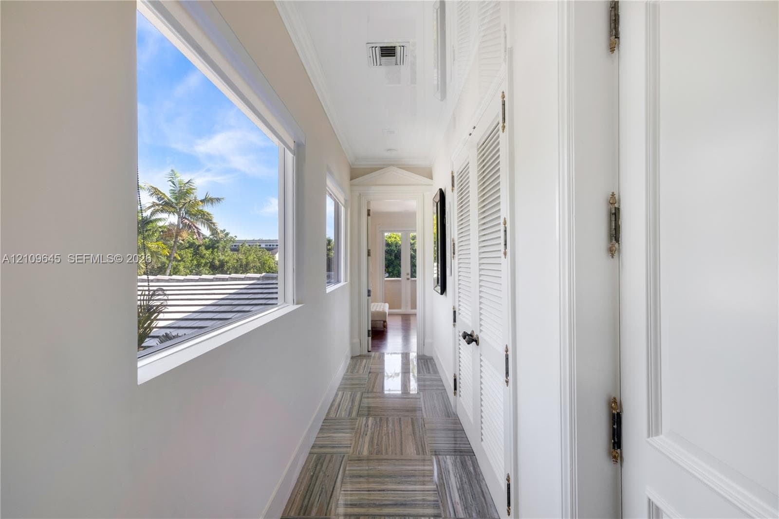 Hallway featuring polished stone flooring, louvered closet doors, crown molding, and large windows