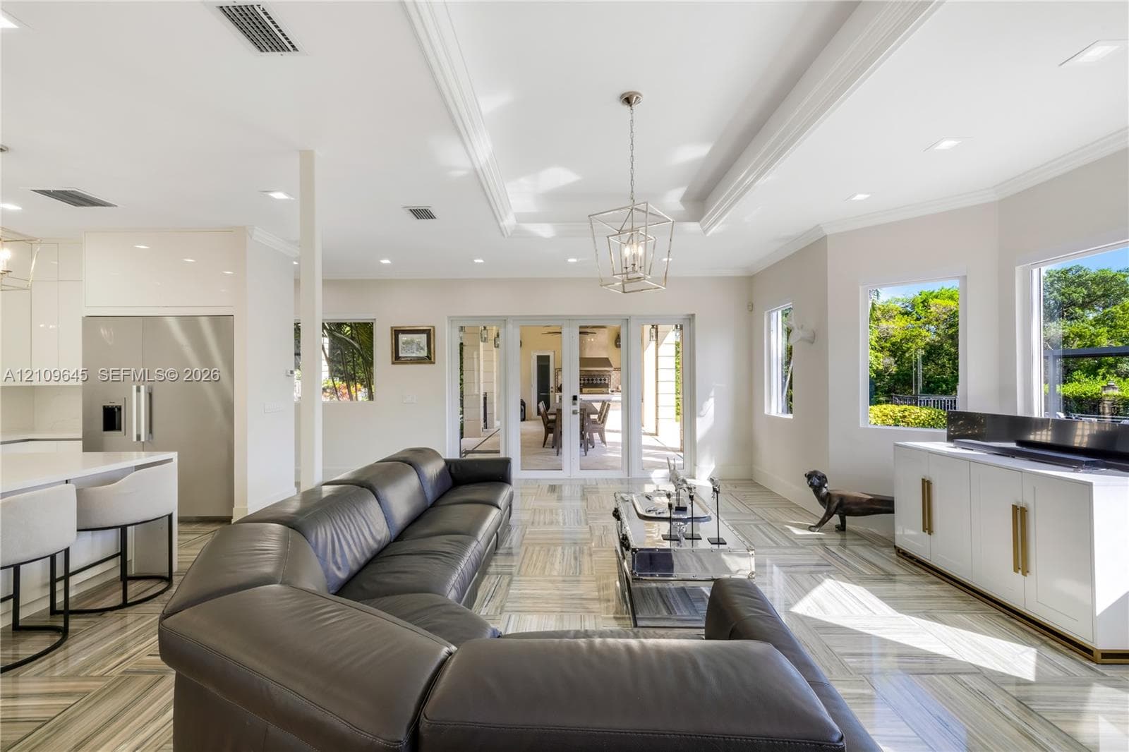 Open-concept living space featuring high ceilings with crown molding, recessed lighting, geometric metal pendant fixture, large-format tile flooring, and glass-paned doors