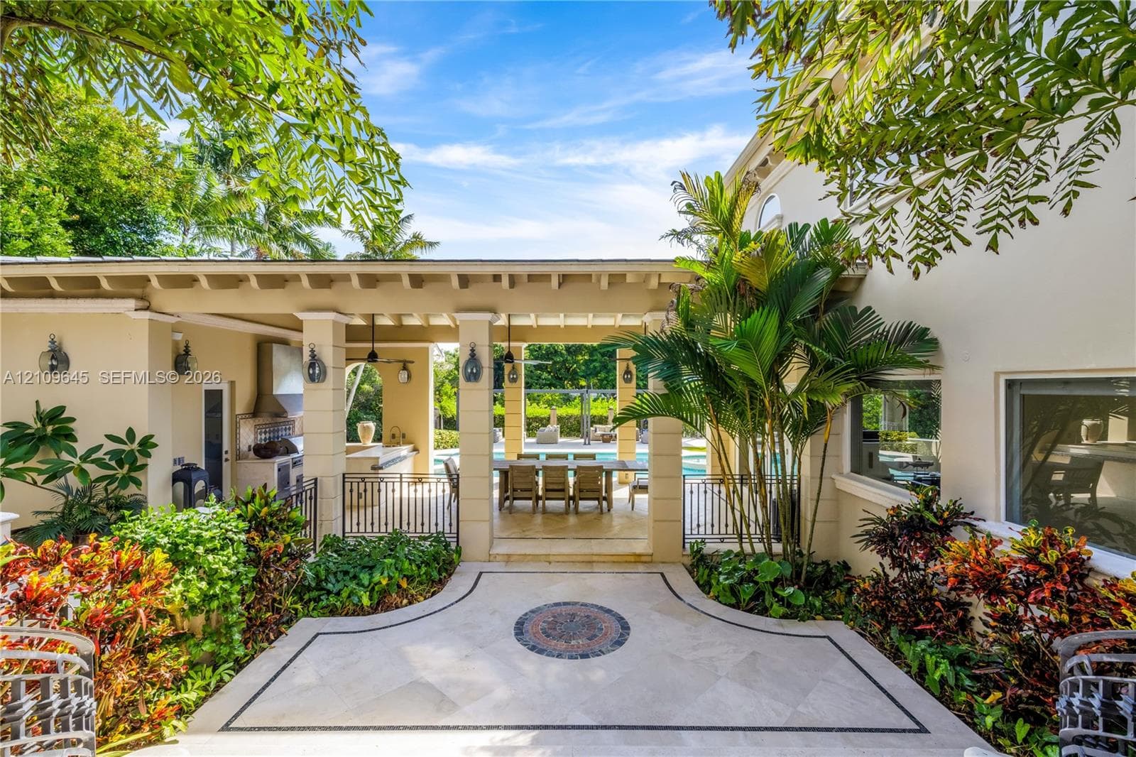 Covered lanai featuring a stone-paver patio with decorative inlay, built-in outdoor kitchen with stainless steel ventilation hood, and heavy-timber beam ceiling