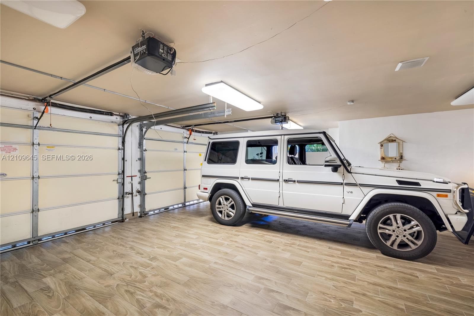 Garage featuring wood-finish flooring, dual motorized garage door openers, and rectangular LED light fixtures
