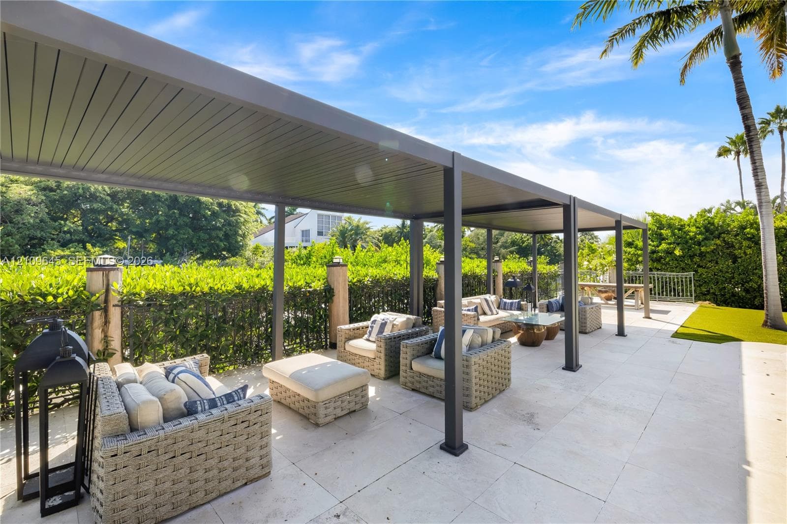 Covered patio featuring a structured metal pergola, large-format stone pavers, and a perimeter of mature privacy hedging