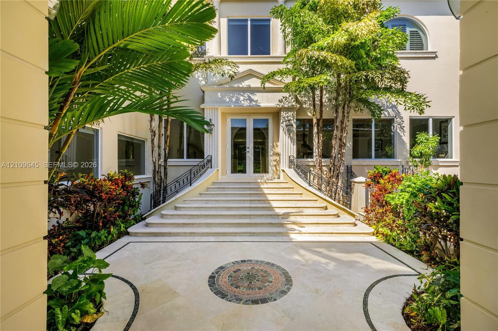 Grand entrance featuring a stone staircase, detailed tile inlay, symmetrical wrought iron railings, and dual glass-paned entry doors