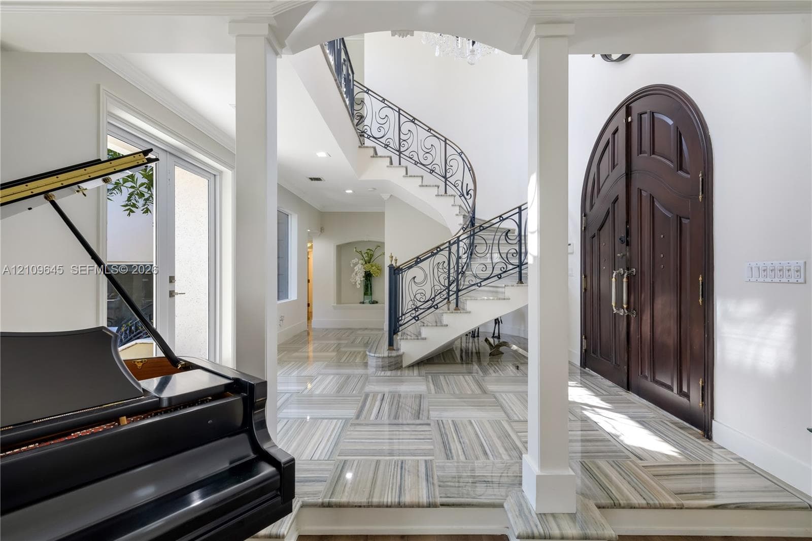 Foyer featuring arched double entry doors, curved staircase with ornamental metal railings, stone flooring with linear patterns, recessed lighting, and a built-in wall niche