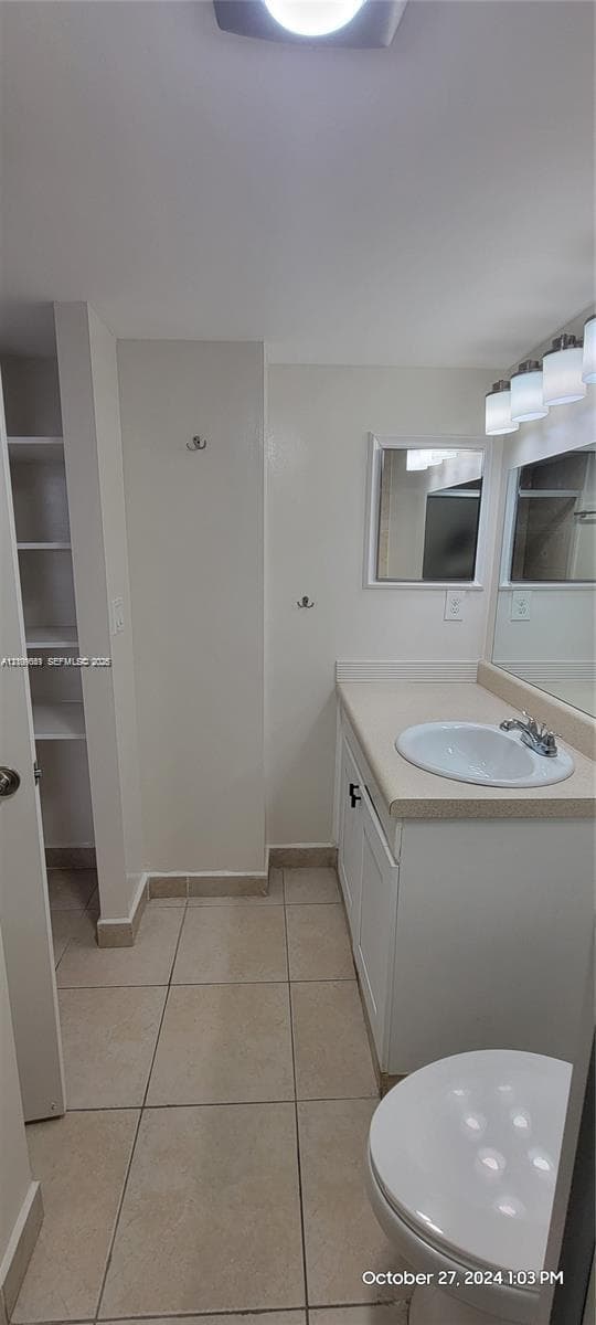 Vanity cabinet with integrated solid-surface countertop and drop-in basin, tiled flooring, wall-mounted mirror, built-in shelving unit, and multi-light fixture