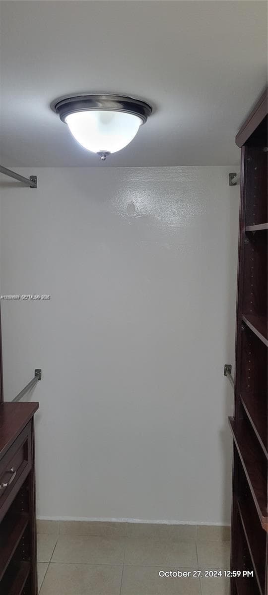 Walk-in closet featuring dark wood-finish built-in shelving, integrated drawers, metal hanging rods, and a ceiling-mounted dome light fixture